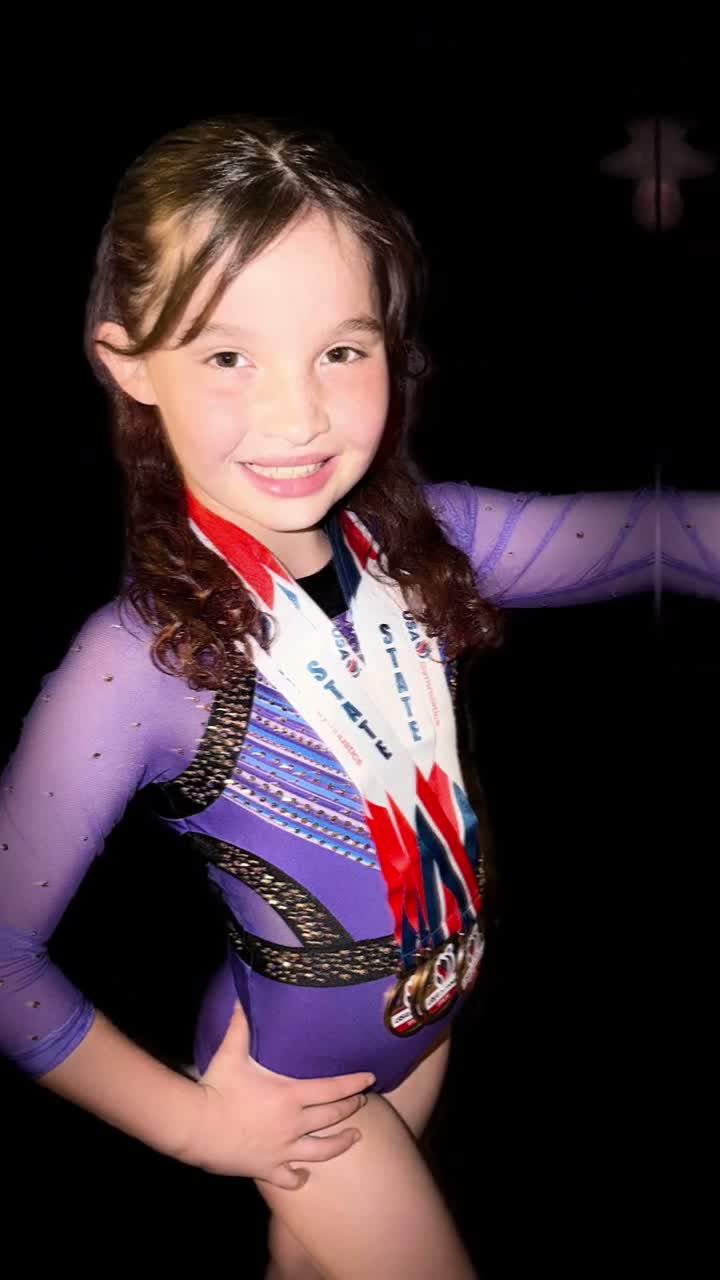 Evie Grace — standing tall in her competition leotard, State medals on, smiling